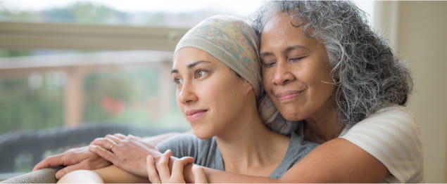 An older adult woman embraces her daughter on the sofa as she gazes out the window.